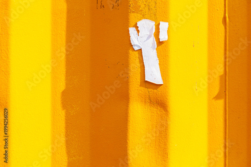 Torn white paper scrap on bright yellow corrugated metal wall