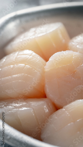 Fresh scallops are piled high in a metal serving dish on a table indoors