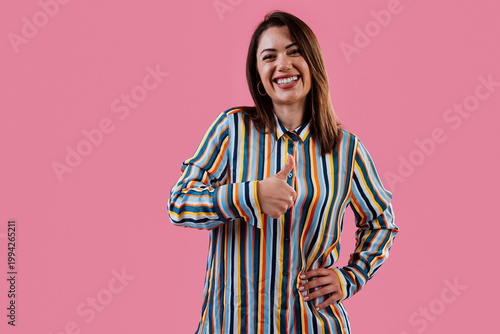 Happy woman giving thumbs up on pink background