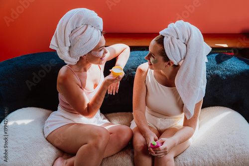 Two women relaxing on sofa with beauty products and towels on heads