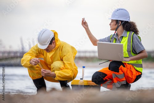 Environmental researchers collecting and examining water samples in test tubes on the coast, Two scientists testing water quality for pollution monitoring using laptop and laboratory equipment