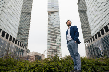 Businessman with hands in pockets standing near modern skyscrapers