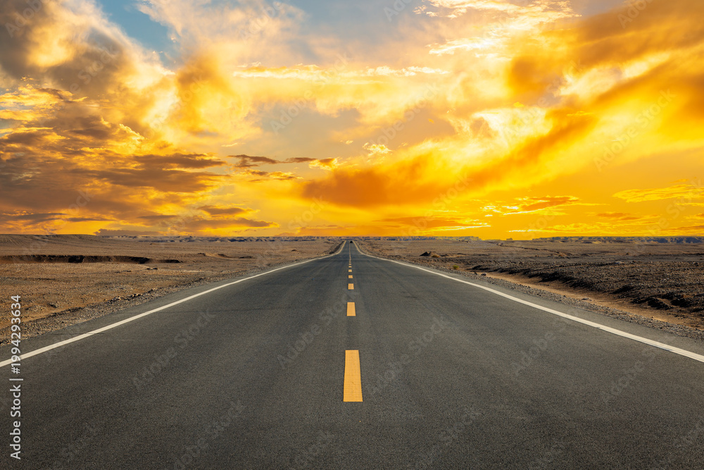 Fototapeta premium Straight asphalt highway through desert landscape under dramatic golden sunset sky, Xinjiang, China