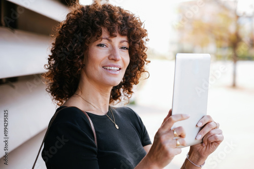 Enthusiastic woman with curly hair sharing bright travel snapshots in lively urban environment
