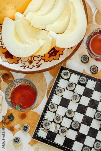 Foto Checkers game board with hand holding piece and sliced fresh yellow melon on flo