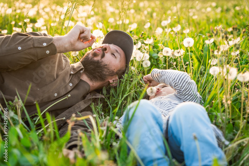 father and daughter playing with dandelions flowers in field at sunset, concept of fatherhood and Parent-child relationships outdoors