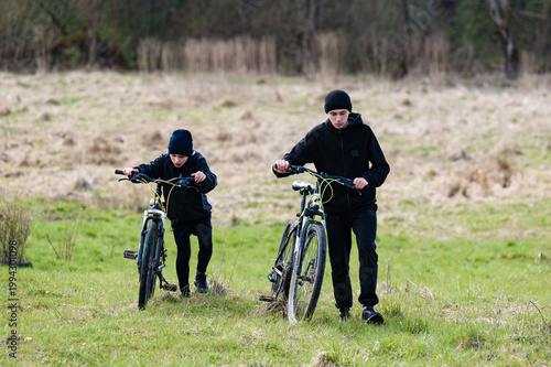 Two boys walk their bikes across a grassy field, enjoying an outdoor adventure.