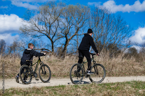 Two boys enjoy a bike ride on a sunny day, along a dirt path. Nature's beauty surrounds them.