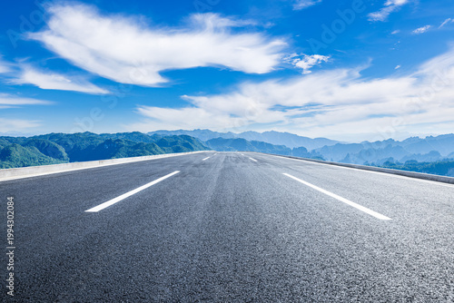 Empty straight asphalt highway leading to a distant mountain range under a blue sky