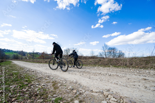 Two cyclists enjoying a sunny day on a gravel road, surrounded by nature. A perfect outdoor adventure.