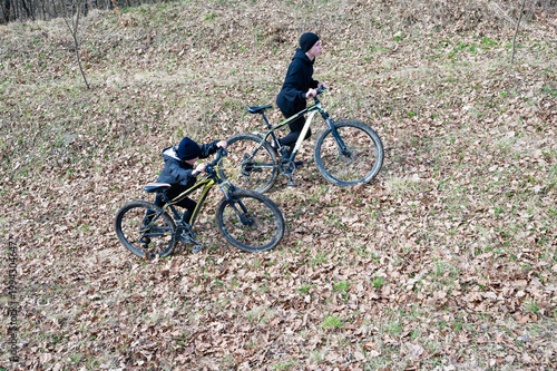 Two cyclists navigate a leaf-strewn path. One helps the other with their bike, showcasing teamwork and outdoor adventure.