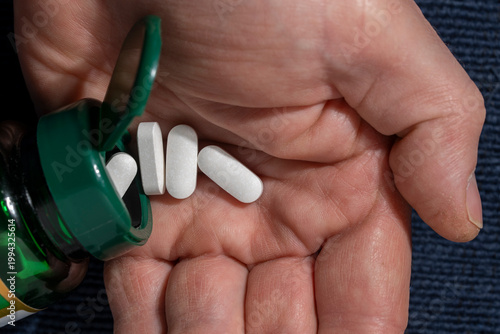 Pouring pills from a bottle into a hand. Closeup of white caplets being poured from green plastic bottle into human palm. Concept of healthcare medication intake supplements or daily vitamin routine