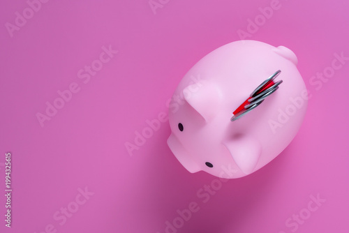 Minimalist top view of a pink piggy bank with silver coins in the slot on vibrant pink surface, copy space. Concept of savings banking financial growth and budget planning