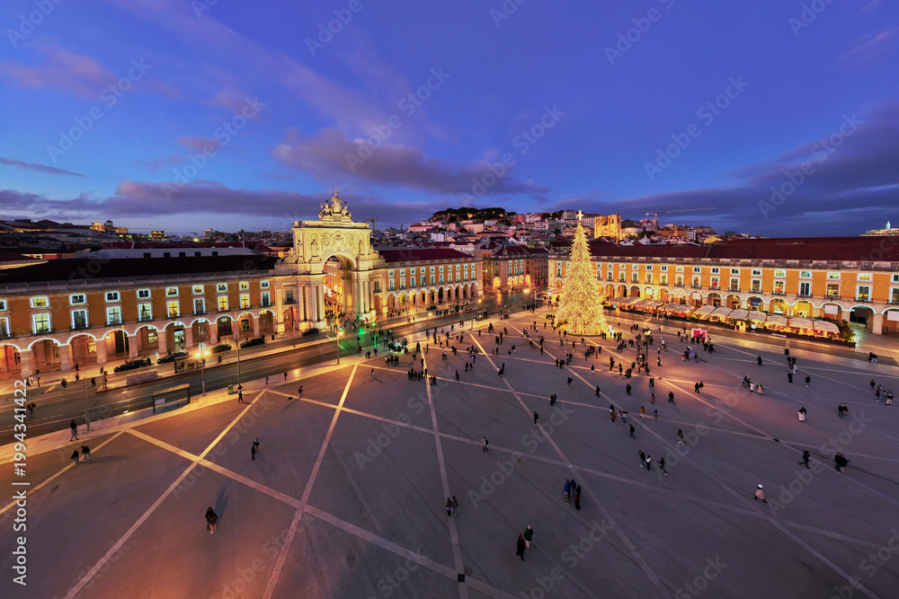 Naklejka premium Praca do Comercio showcases a stunning Christmas tree and decorations, captivating visitors in the evening light of winter.