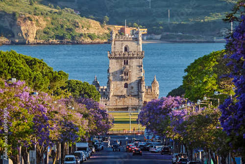 Tableau sur toile Enjoy a scenic sunset view of Belem Tower overlooking the Tagus River, surrounded by vibrant jacaranda trees in full bloom