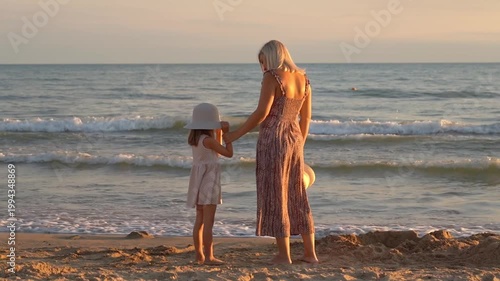 Mother and daughter look at sea on sand beach at sunset. Happy family walk by ocean. Summer vacation travel holiday