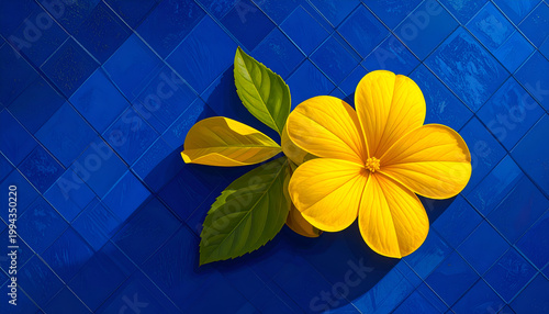 A vibrant yellow flower with lush green leaves rests gracefully on a striking blue tiled surface, creating a visually appealing contrast of colors and textures.