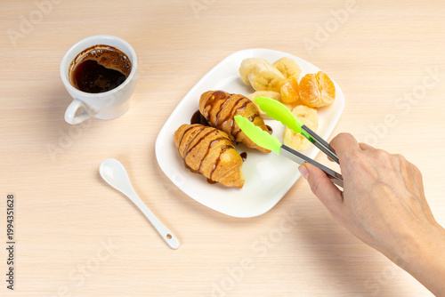 Cup of black coffee, tropic fruits and fresh croissants on the kitchen table.