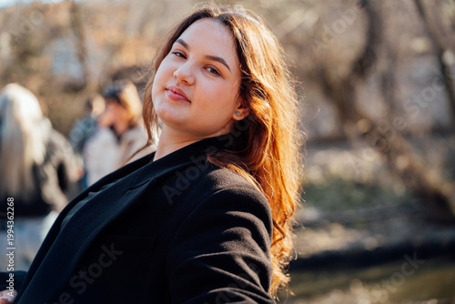 Fotografia Young woman of caucasian appearance posing outdoors in park near water with sunlight and soft background blur