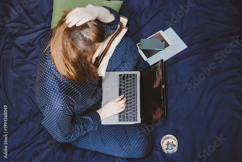 asian woman in classic blue pajama cloth work from home and sit on her bed for protect corona or covid-19 virus