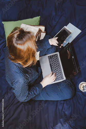 asian woman in classic blue pajama cloth work from home and sit on her bed for protect corona or covid-19 virus