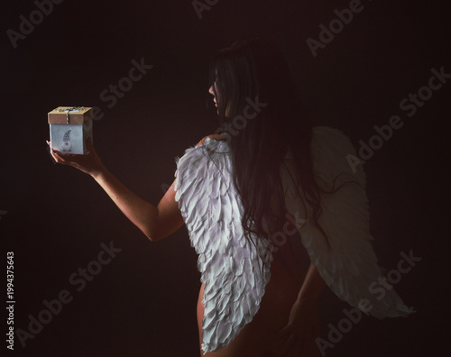 Frau mit Engelsflügeln hält Geschenk – Weihnachten, Geburtstag, Engel, Licht, Emotion, festliche Stimmung, Überraschung, Symbolik, Studio, Copyspace, isoliert