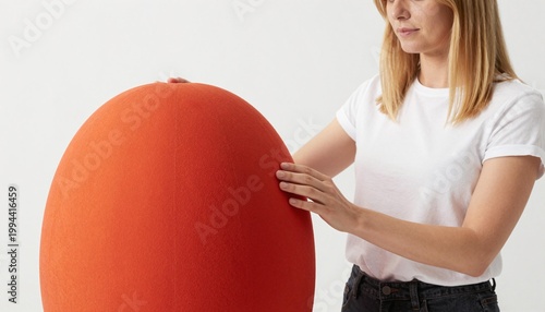 Woman adjusting a large bright orange egg-shaped upholstered chair against a neutral backdrop