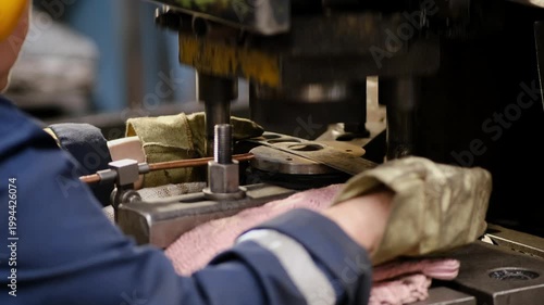 Close up of a factory worker using protective gloves to operate a large industrial metal pressing machine during production process.