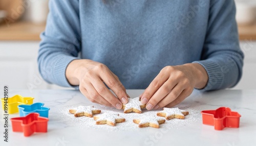 Person dusting powdered sugar onto star-shaped cookies on a kitchen counter