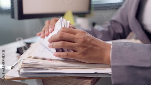 Close up of businesswoman sorting stack of documents at office desk with computer in background. Concept of paperwork organization, document sorting, office administration, and workflow efficiency.