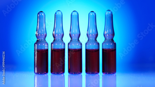 Test tubes with red liquid stand in a row under blue light in a lab setting during the day