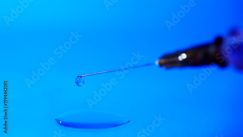 Close up of a syringe with a droplet of liquid on a blue surface in a clinical setting during laboratory work