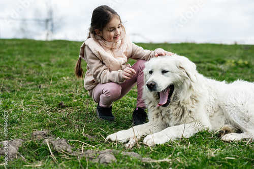 Young girl gently petting a large white dog on a grassy field while smiling and bonding during an outdoor spring day