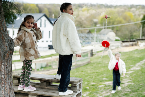 Three children playing outdoors in the countryside wearing warm coats and sneakers on a wooden platform