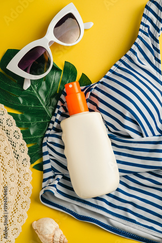 Sunscreen skin protection. Summer holiday flat lay yellow background. Beach travel accessories for vacation. Sunglasses, sun hat, swim suit, sunscreen.