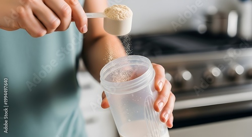 Person pouring a scoop of protein powder into a shaker bottle in the kitchen