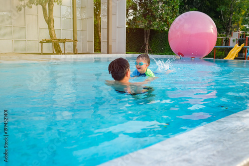 Asian father and son playing in swimming pool, child wearing goggles learning to swim, happy family bonding outdoors, summer activities, lifestyle, fun water splash