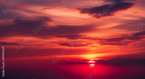 dramatic sunset with fiery orange and deep red clouds, sun low on horizon with radiant glow, dramatic atmosphere, perfect for nature backgrounds
