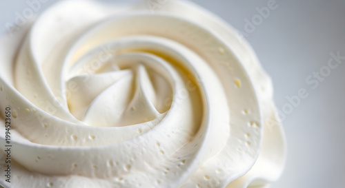 Close up of creamy white frosting swirled into a rosette shape, delicate texture with small bubbles, perfect for baking and dessert concepts