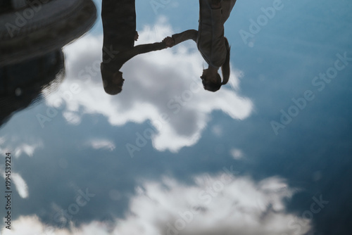 Slika na platnu A couple holds hands seen as a reflection in a puddle against a cloudy sky