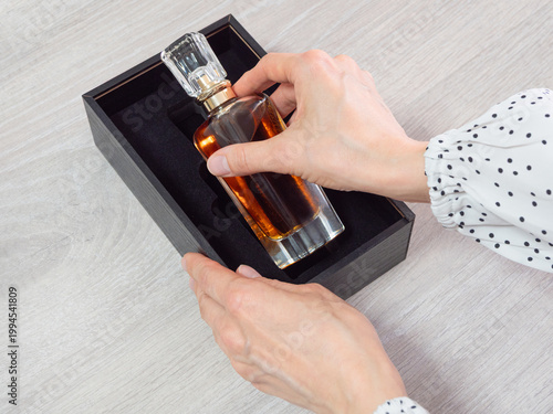 Elegant hands place a glass perfume bottle into black gift box