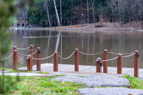  Tranquil scene featuring a serene pond in a park, bordered by lush trees and highlighted by a wooden bridge. The reflective water creates a peaceful ambiance suitable for relaxation.