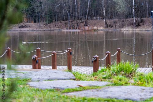  Tranquil scene featuring a serene pond in a park, bordered by lush trees and highlighted by a wooden bridge. The reflective water creates a peaceful ambiance suitable for relaxation.