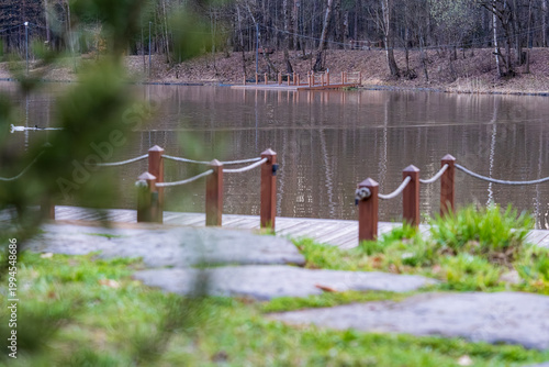  Tranquil scene featuring a serene pond in a park, bordered by lush trees and highlighted by a wooden bridge. The reflective water creates a peaceful ambiance suitable for relaxation.
