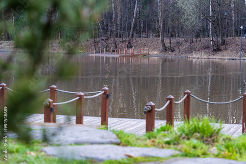  Tranquil scene featuring a serene pond in a park, bordered by lush trees and highlighted by a wooden bridge. The reflective water creates a peaceful ambiance suitable for relaxation.