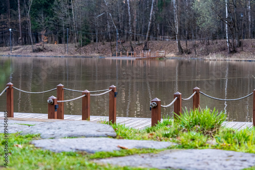  Tranquil scene featuring a serene pond in a park, bordered by lush trees and highlighted by a wooden bridge. The reflective water creates a peaceful ambiance suitable for relaxation.