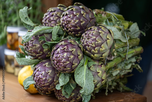 A large bunch of fresh Romanesco artichokes displayed on a wooden market stall.