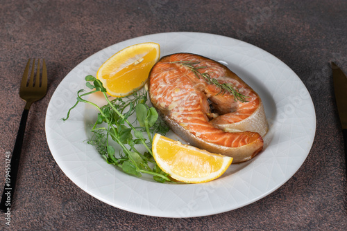 Photos Baked trout steak with lemon, rosemary and garlic on white plate