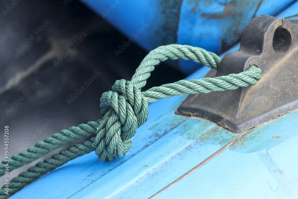 Fototapeta premium Close up green rope tied in secure knot attached to blue inflatable rubber boat showing nautical maritime safety equipment evoking reliable sturdy feeling outdoors