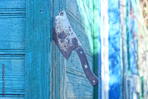 one old rusty iron cleaver axe sticks out of a green wooden wall on a daytime street